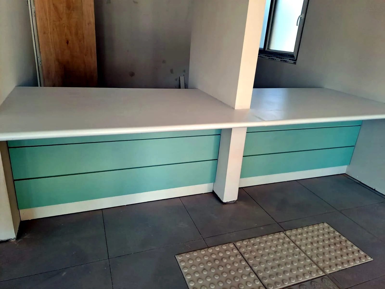 Mesón de atención blanco en L con frente de paneles verde agua y repisa alta