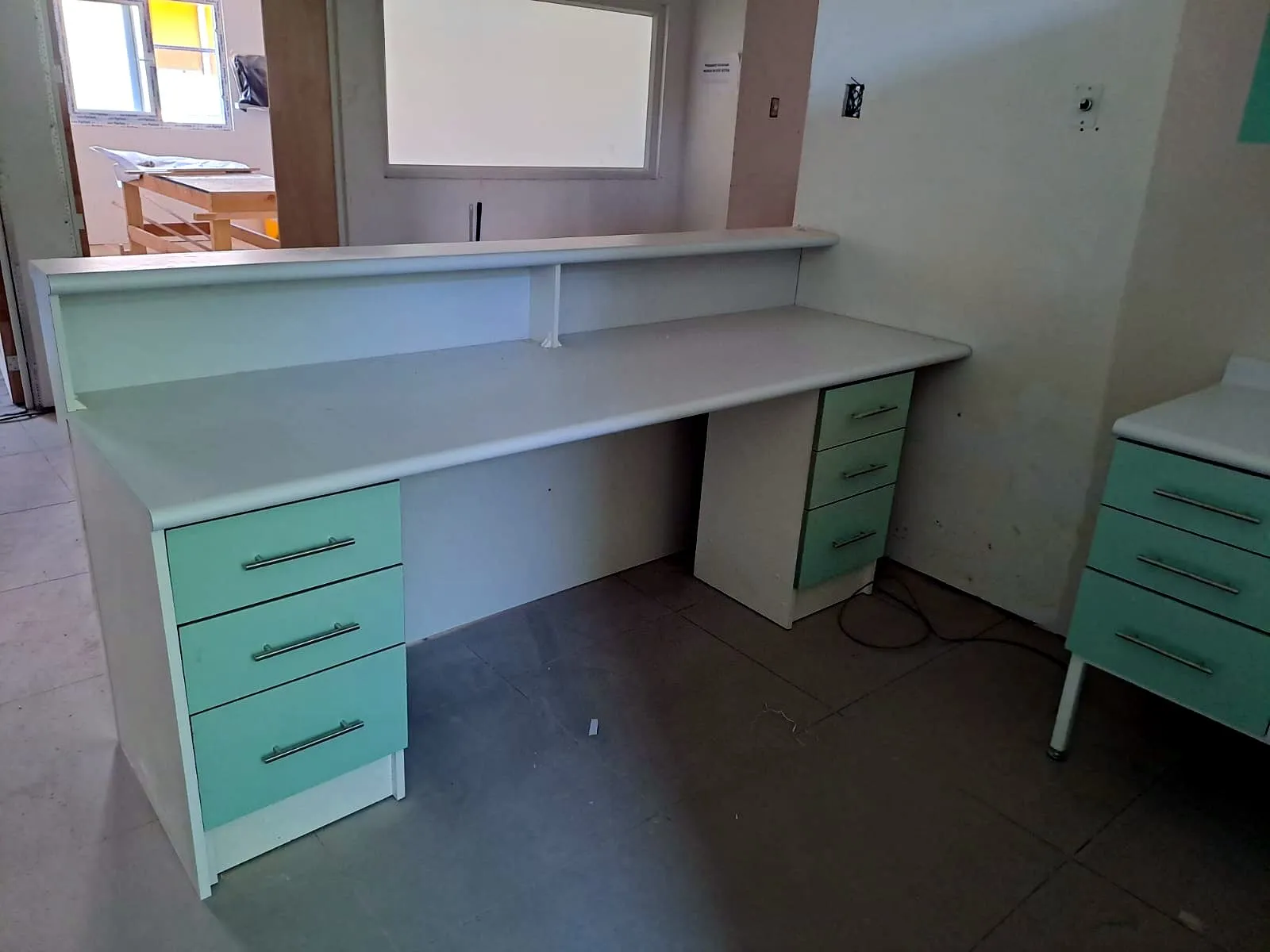 Mesón de atención blanco con repisa alta y dos cajoneras con cajones verde agua