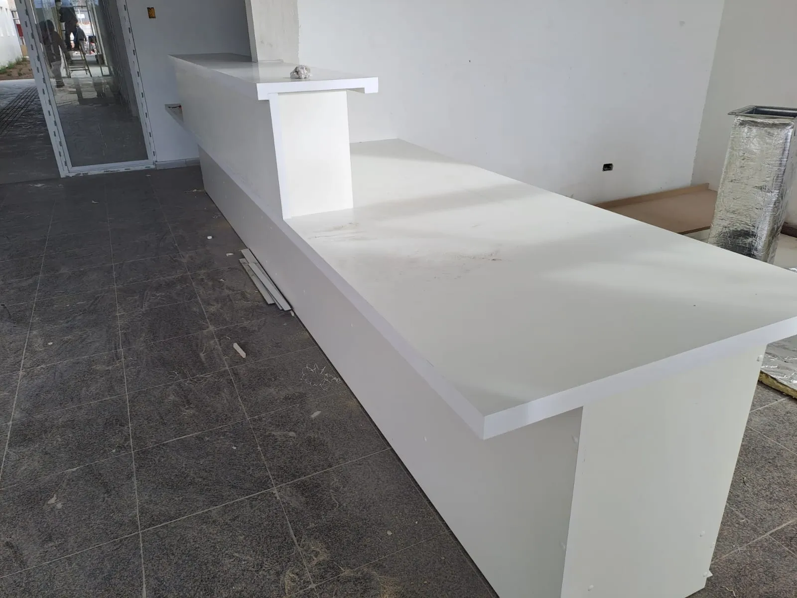 Mesón de atención largo en blanco, con cubierta postformada y repisa alta, recién instalado en un local en obra