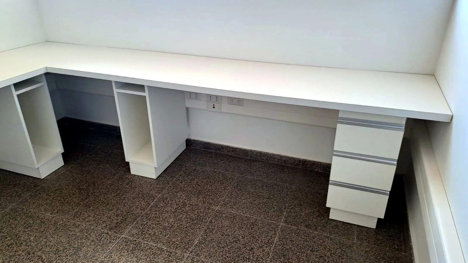 Escritorio corrido blanco a lo largo del muro, con cajonera y espacio para CPU